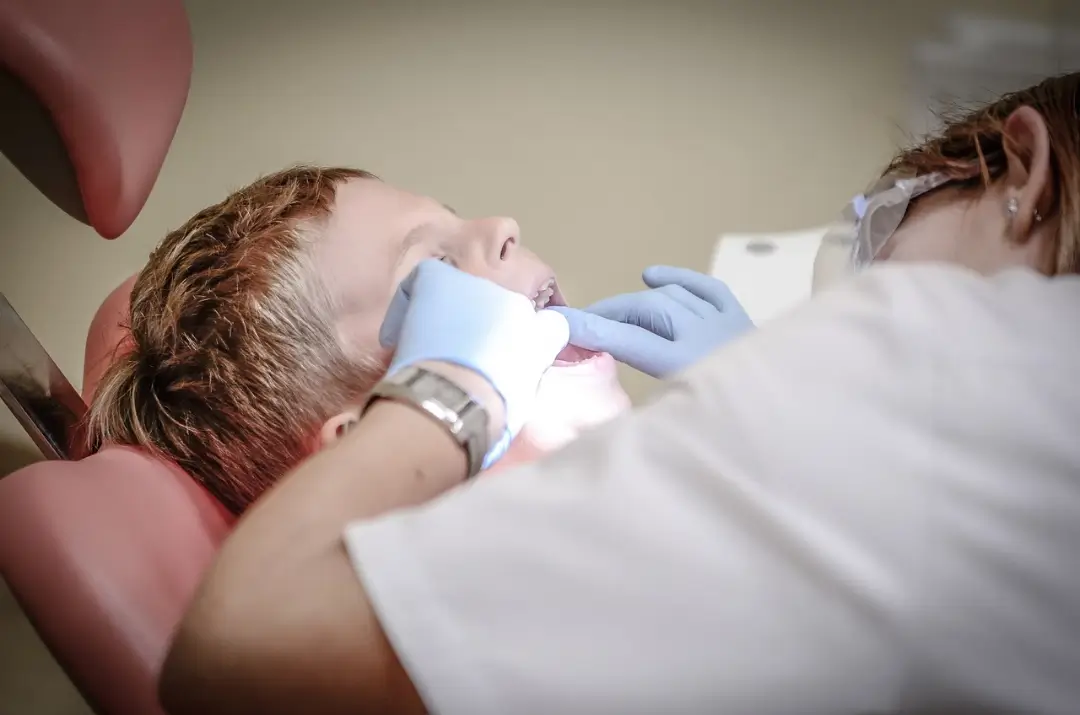 Un profesional dental con guantes realiza un examen a un paciente reclinado en un sillón dental, con una iluminación superior brillante.