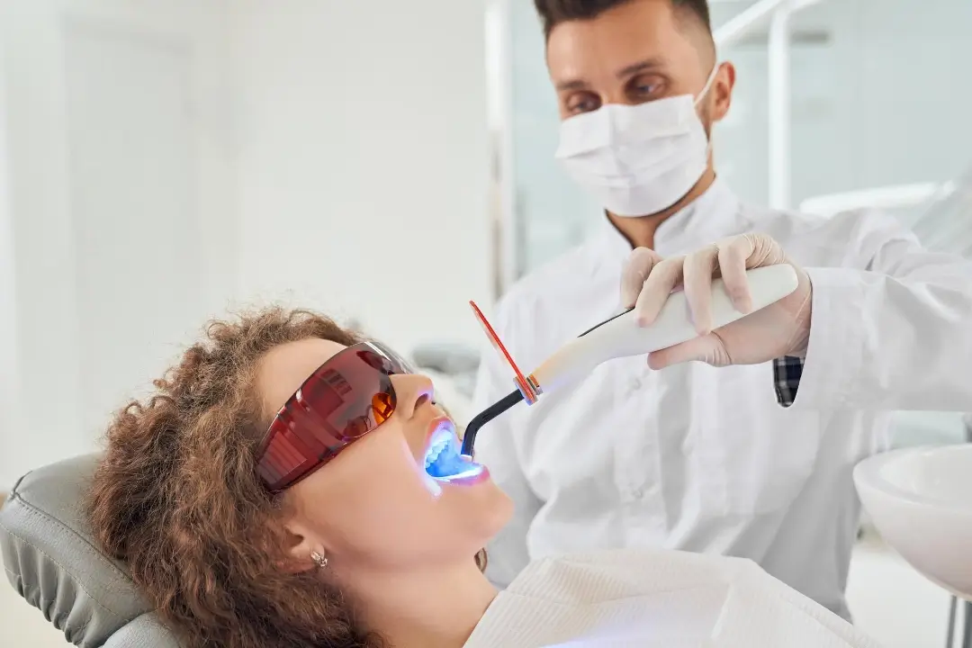 Un dentista con bata blanca utiliza una herramienta dental en un paciente reclinado en una silla, rodeado de un entorno clínico moderno.