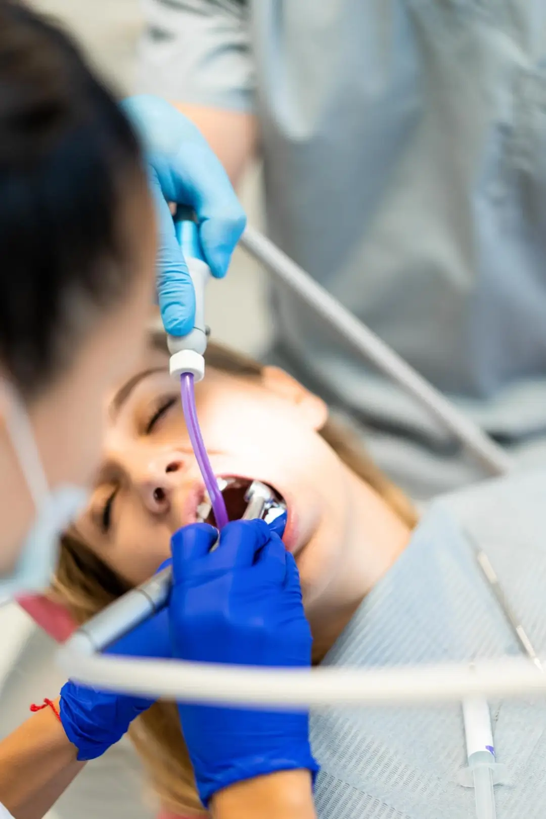 Un profesional dental examina la boca de un paciente, utilizando un espejo dental, mientras usa guantes azules en un entorno clínico.